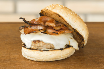 homemade hamburger with cheese and bacon over wooden cutting board and brick background
