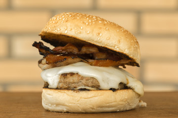 homemade hamburger with cheese and bacon over wooden cutting board and brick background