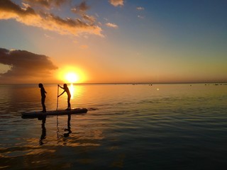 Two little girls do stand up paddling in the lagoon of Moorea during sunset, Moorea, Tahiti, French Polynesia