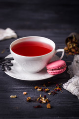 Fruit tea and pink raspberry macaron on black wooden background. Traditional French sweets