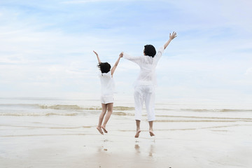 Fototapeta na wymiar Relaxing Asian family time during summer vacation. Asian Mother with daughter holding hands, having fun and jumping on beach.