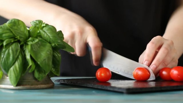 Close-up of woman hand cutting tomatoe on black stone