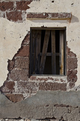 Eine alte Wand mit einem Fenster, das teilweise mit Brettern verriegelt ist.