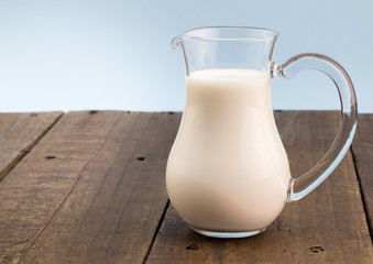 Fresh whole milk in glass jug on rough wooden table background