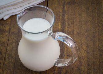 Natural whole milk in glass jug on rustic wooden table
