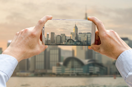 Cropped Shot View Of Man's Hands Making Photo On Mobile Phone Camera Of Building In Hong Kong Against Beautiful Sunrise.