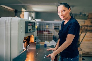 Worker in printing centar uses paper guillotine machine knife