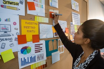 Female executive writing on sticky note at bulletin board