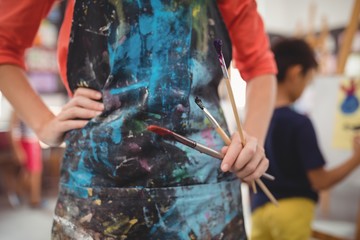 Mid section of teacher standing with paintbrushes