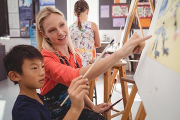 Teacher assisting schoolboy in drawing class