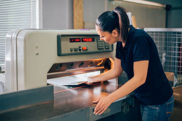 Worker in printing centar uses paper guillotine machine knife