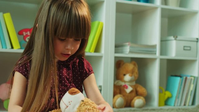 Beautiful little girl take care abiut her teddy bear. Litte girl hugging toy bear while playing in kids room. Close up