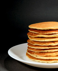 Vertical photo of fresh homemade plain pancakes stack served on white plate on black background 