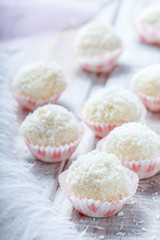 Homemade white truffles candy dessert sprinkled in coconut chips on wooden background close up. Delicious chocolate praline
