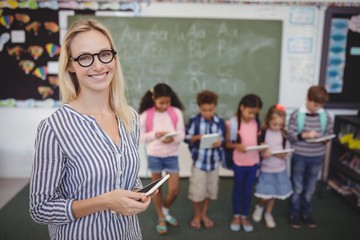 Portrait of happy teacher standing holding digital tablet