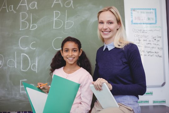 Portrait of smiling teacher and schoolgirl in classroom