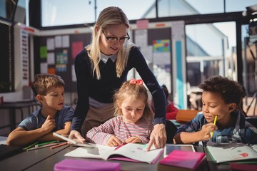 Teacher helping schoolgirl with her homework in classroom