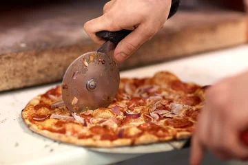 Zelfklevend Fotobehang cook hands cutting pizza to pieces at pizzeria © Syda Productions