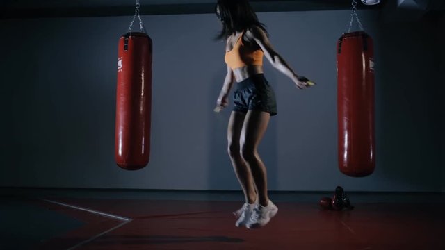 Young woman boxer jumping on a skipping rope in a dark hall