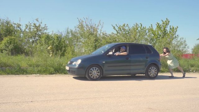 Young woman  in green dress pushing a car while man is emboldening her.Transportation, teamwork, funny concept