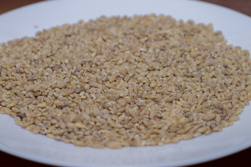 Pearl barley in a white plate. Wooden background
