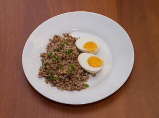 Buckwheat and two boiled eggs on a white plate. Wooden background