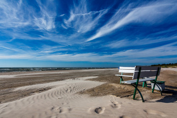 Bench on a white sand beach with blue dark blue sky.