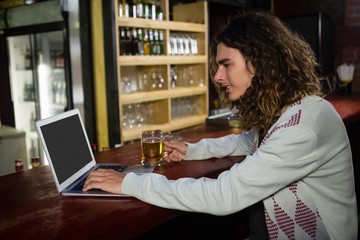 Man having beer while using laptop at counter
