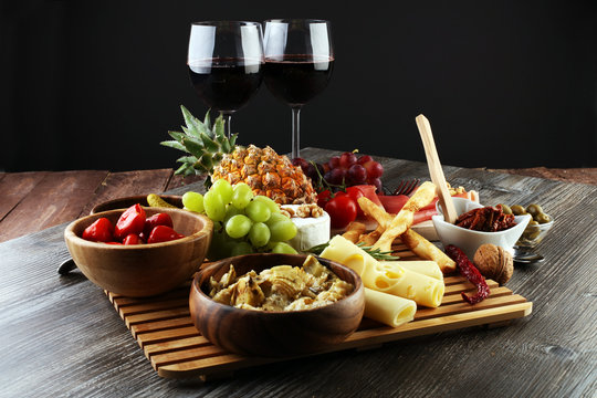 Italian antipasti wine snacks set. Cheese variety, Mediterranean olives, pickles, Prosciutto di Parma with grapes, wine in glasses over black grunge background