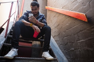 Man using mobile phone while having drink on staircase