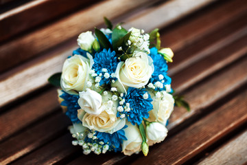 Wedding bouquet of white roses and blue chrysanthemums on a brown wooden bench, a bouquet of the bride