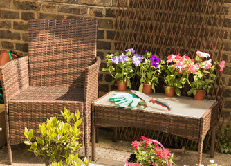 Fototapeta na wymiar Garden tools, gloves and flower plants from a garden center are lying on a table near from armchair in a garden. 