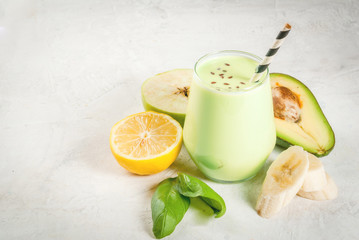 Fototapeta premium Healthy food. Dietary breakfast or snack. Green smoothies from yoghurt, avocado, banana, apple, spinach and lemon. On white concrete stone table, with ingredients. Copy space