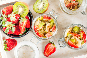 Healthy breakfast. Diet. Overnight oatmeal in a can, muesli. Yogurt with homemade granola and organic fruits - kiwi, banana, strawberry. On tray on stone table.  Copy space close top view
