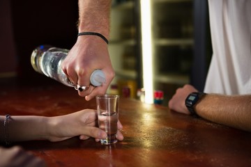 Mid section of bartender serving tequila to customer