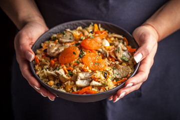 The girl cook holds a plate with a vegetarian plov, Uzbek traditional cuisine