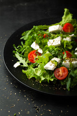 Fresh salad with cherry, arugula, feta, basil and olive oil in a plate