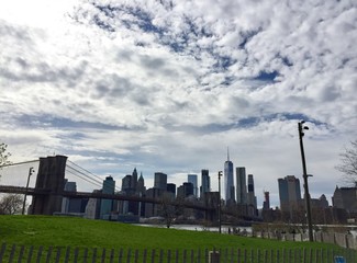 Fototapeta na wymiar Brooklyn bridge and buildings in Manhattan under cloudy sky at Brooklyn bridge park