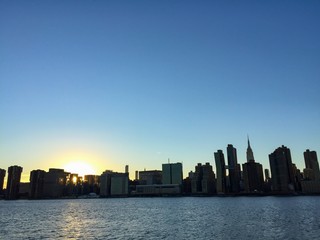 Silhouette of buildings in Manhattan with sunset and river, New York