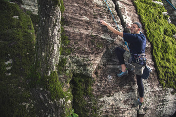 A young hipster is engaged in rock climbing with insurance on rocks with green moss