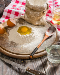 Ingredients for cooking dough or bread. Broken egg on top of a bunch of white rye flour. Dark wooden background.