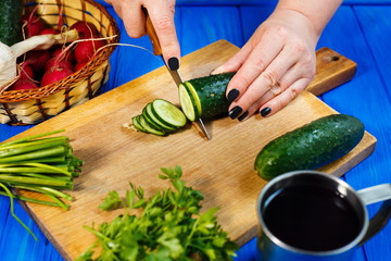 Woman hands cutting fresh crunchy cucumber on cutting board with spring onions and herbs on the foreground
