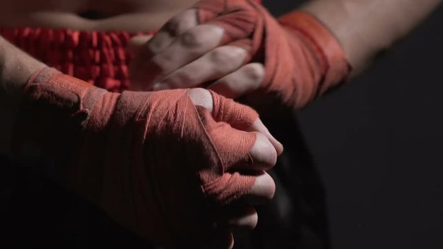 Muay Thai professional boxer adjusting bandages on his hands before fight, sport