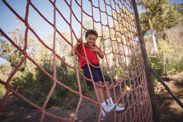 Portrait of happy boy climbing a net during obstacle course
