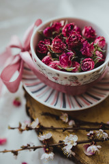 A cup with a saucer filled with roses and a pink bow