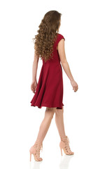 Woman In Elegant Burgundy Dress Is Walking. Side Rear View.