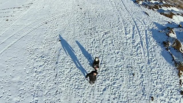 Aerial. Dad rolls his son fast on a sled. Dady and his baby have fun. Man running on snow.
