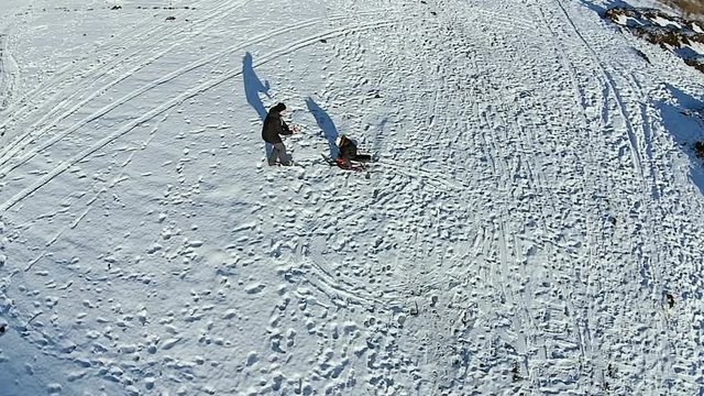 Aerial. Dad rolls his son on a sled and shoots a video. Dady and baby have fun. Man playing with boy.