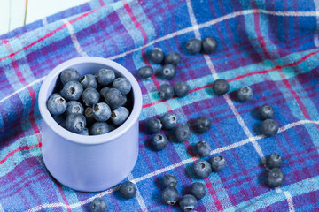 Blueberries in cup. Blue wooden table, blue kitchen towel.
