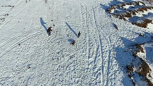 Aerial. Dad rolls his son on a sled and shoots a video. Dady and baby have fun.